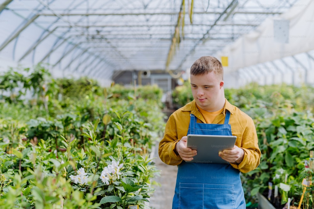 Un jeune employé trisomique travaillant dans une jardinerie, tapant sur une tablette.