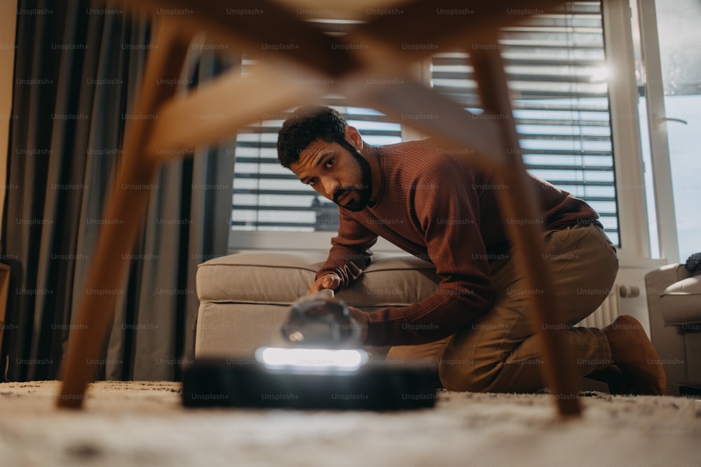 A young man hoovering carpet with vacuum cleaner in living room