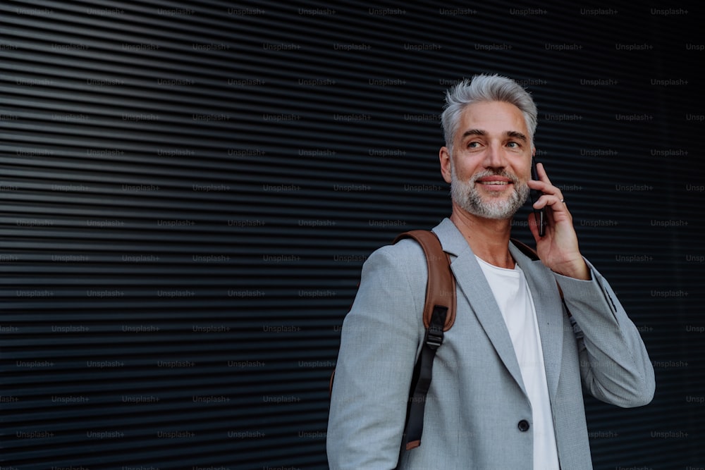 成功した幸せなビジネスマンは、街の通りで待っている、携帯電話で電話をかけ、通勤のコンセプト。