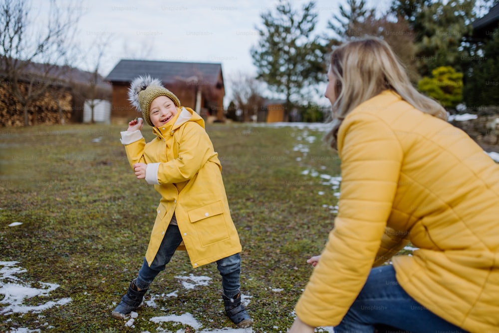 A boy with Down syndrome with his mother playing with snow in garden.