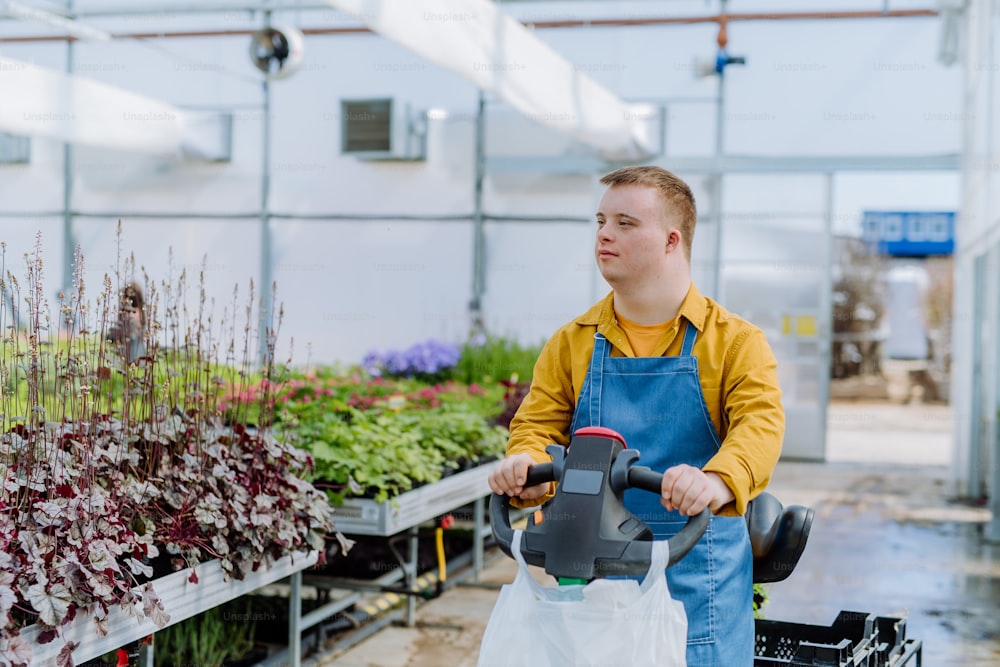 Un jeune employé atteint du syndrome de Down travaillant dans une jardinerie, à l’aide d’un gerbeur de palettes manuel.