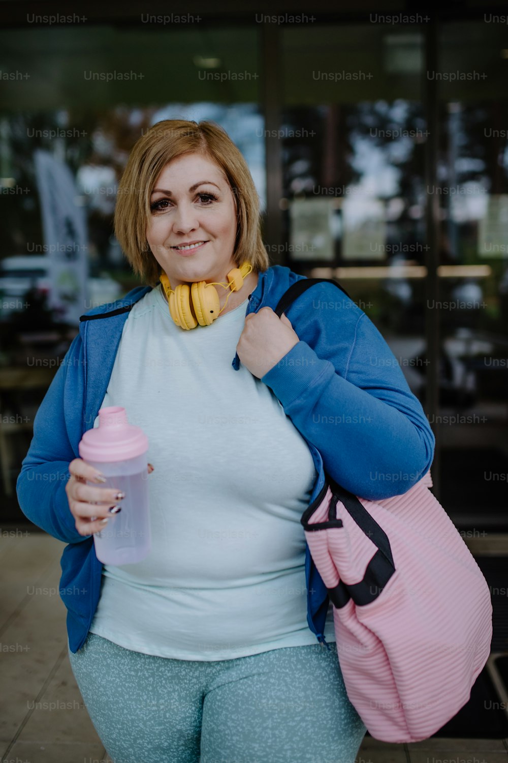 운동복을 입은 행복한 과체중 여성이 피트니스 센터 앞에서 야외에서 카메라를 보고 있다