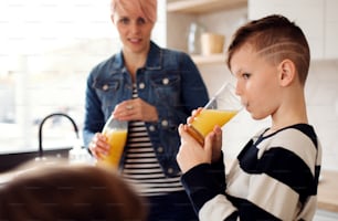 A young woman with happy children drinking orange juice in a kitchen.