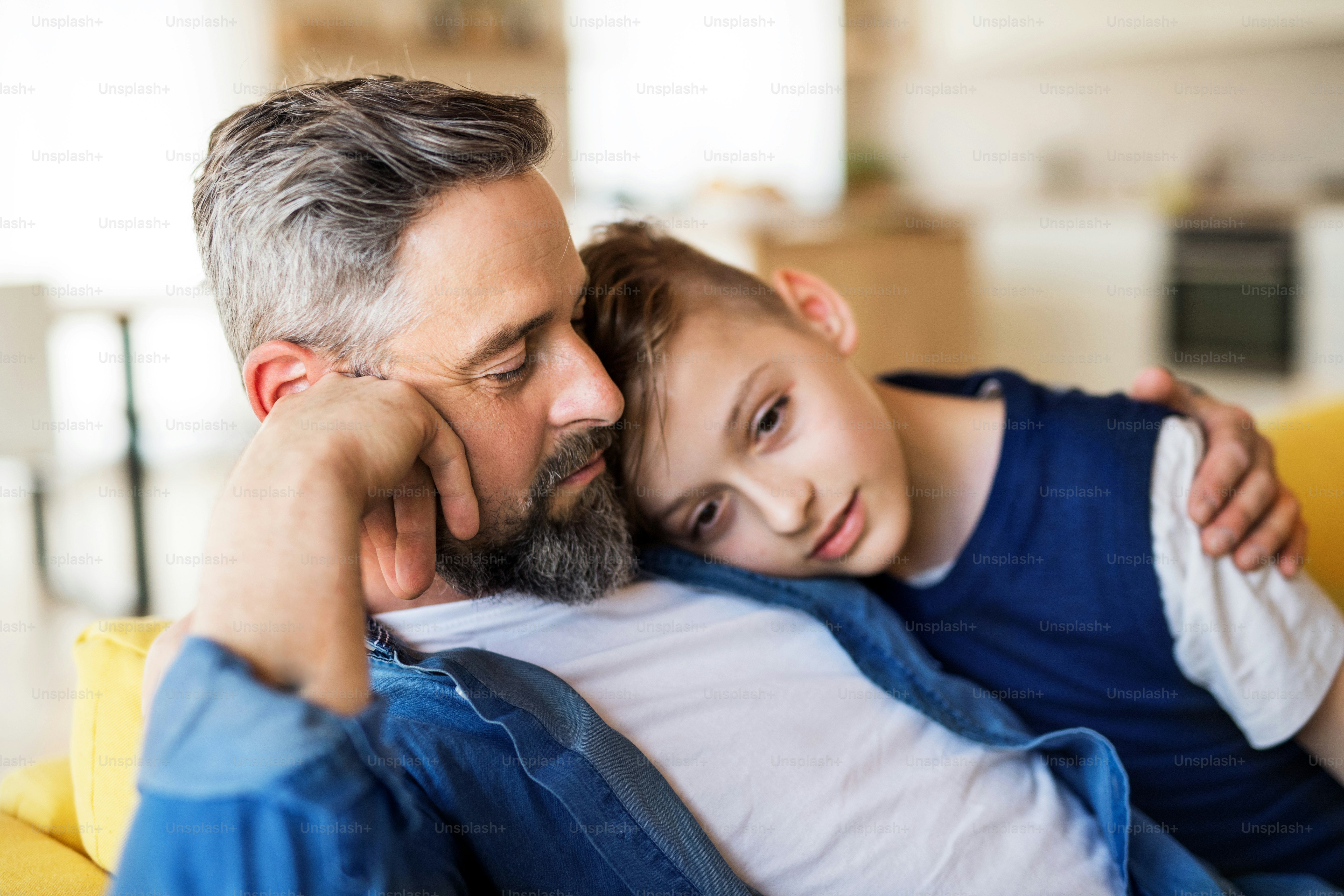 A mature father with small son sitting on sofa indoors, resting.