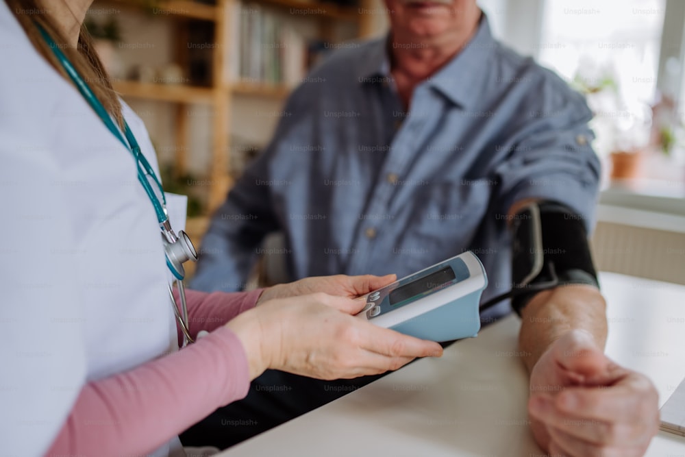 Uma médica visitante homem idoso e examiná-lo dentro de casa em casa, medindo a pressão arterial.