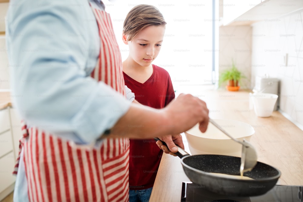 Ein Mittelteil des reifen Vaters mit kleinem Sohn drinnen in der Küche, der Pfannkuchen macht.