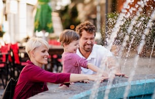 Des parents avec deux petites filles s’amusent à l’extérieur près d’une fontaine en ville.