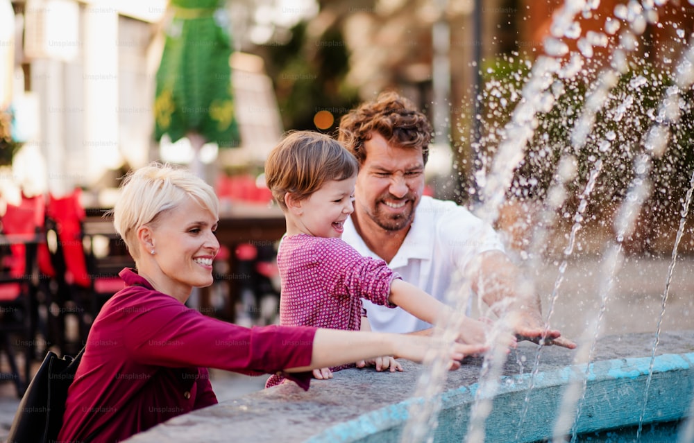 Parents with two small daugther having fun outdoors by fountain in town.