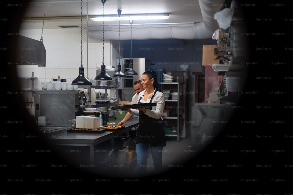 A happy chef and cook working on their dishes in restaurant kitchen, shot through circle door window.