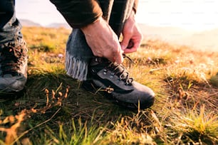 美しい秋の自然の中を散歩するアクティブなシニア男性。靴紐を結んでいる見分けのつかない男。クローズアップ。