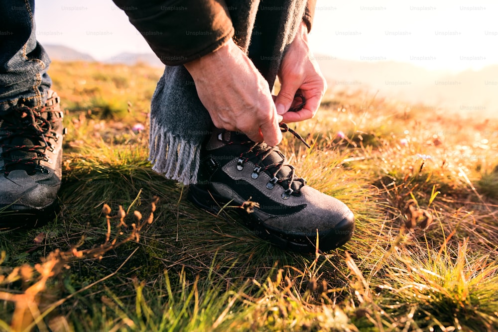 Hombre mayor activo en un paseo en una hermosa naturaleza otoñal. Hombre irreconocible atándose los cordones de los zapatos. Cerrar.