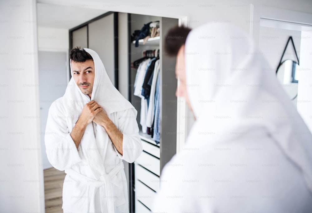 Giovane uomo con accappatoio che asciuga i capelli in camera da letto, una routine mattutina.