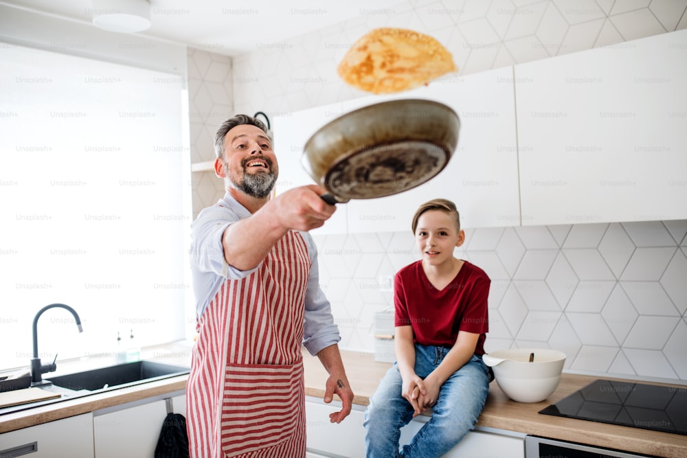 Un padre maturo con un figlio piccolo in casa, in cucina, che gira frittelle.