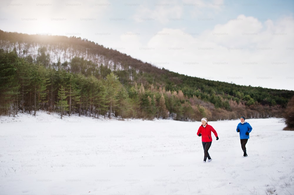 Couple de personnes âgées faisant du jogging à l’extérieur dans la nature hivernale.