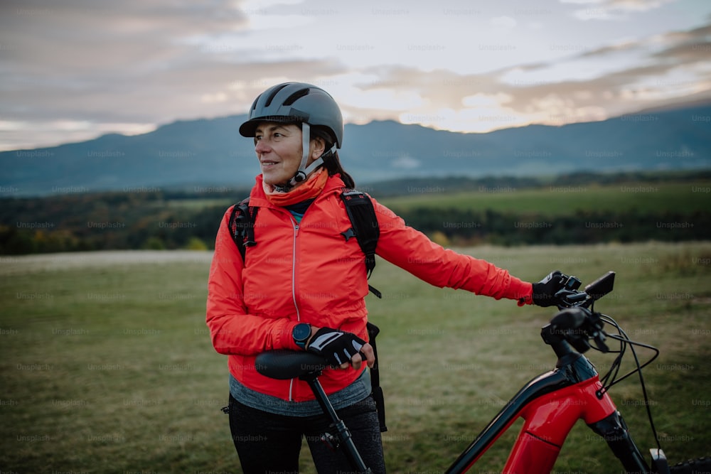 A senior woman biker standing with bike outdoors in nature in autumn day.