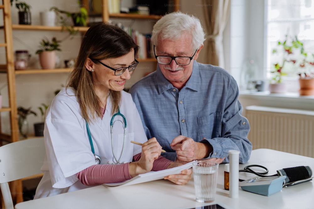 Un travailleur de la santé ou un soignant rend visite à un homme âgé à l’intérieur à la maison, expliquant la posologie du médicament.
