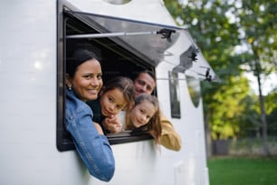Una familia joven y feliz con dos niños mirando por la ventana de la caravana.