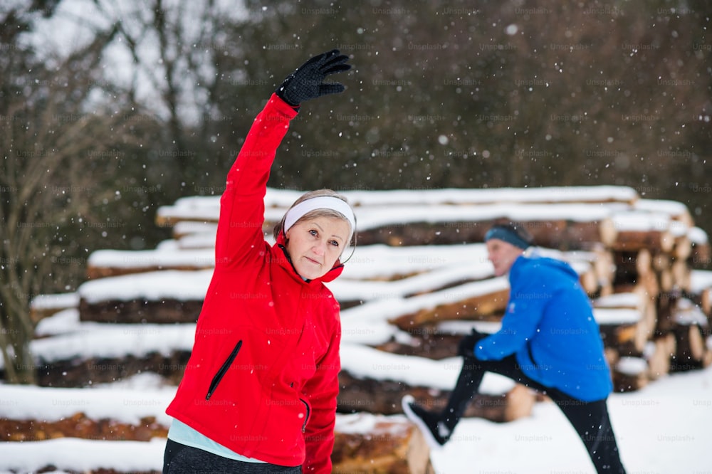 冬の自然の中で外でジョギングし、ストレッチをするシニアカップル。