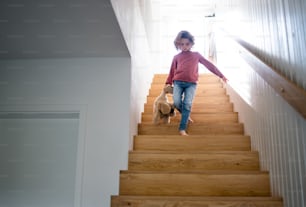 Eine Vorderansicht eines süßen kleinen Mädchens, das zu Hause die Holztreppe hinuntergeht.