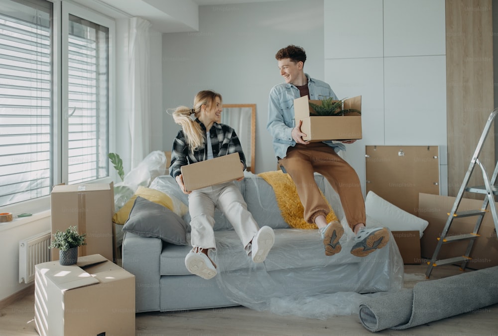 Ein fröhliches junges Paar in ihrer neuen Wohnung, Kisten tragend. Konzeption des Umzugs.