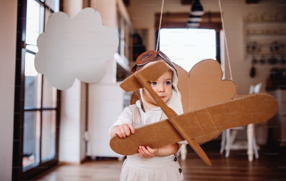 A toddler girl with carton plane and clouds playing indoors at home, flying concept.