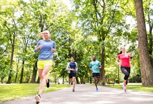 Grupo de jovens atletas correndo no parque de verão verde ensolarado.