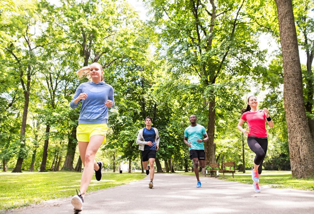 Group of young athletes running in green sunny summer park.