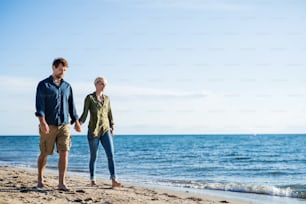 A young couple walking outdoors on beach, holding hands. Copy space.
