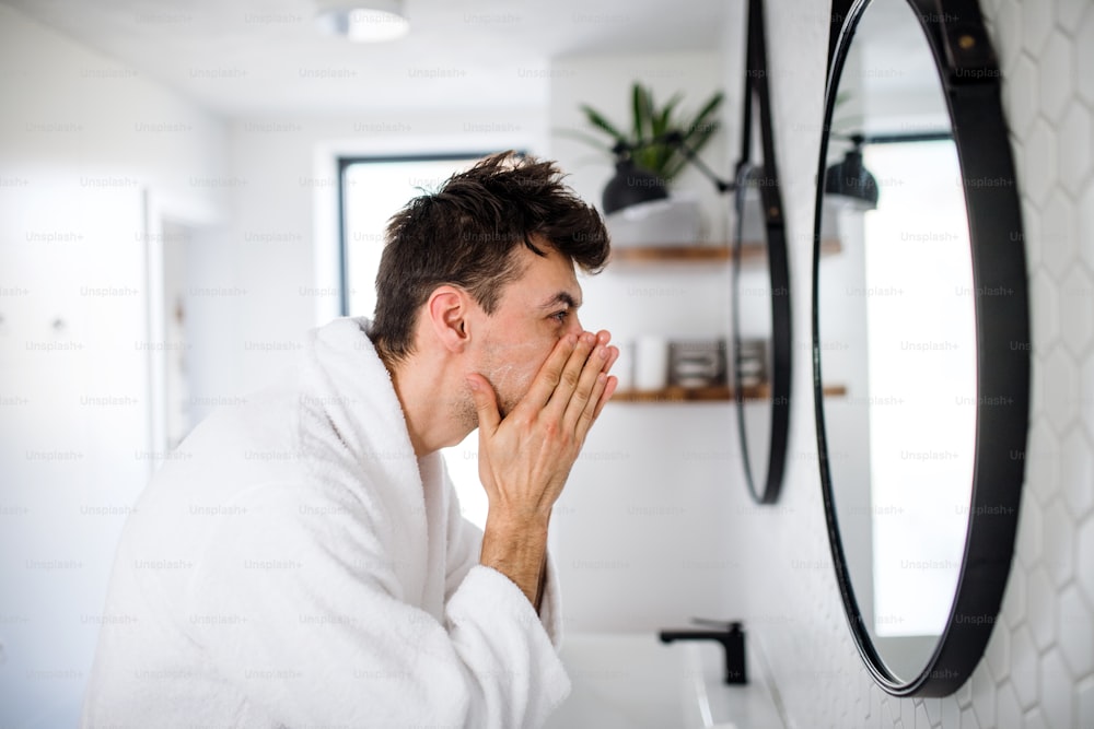 Junger Mann, der morgens im Badezimmer das Gesicht wäscht, eine tägliche Routine.