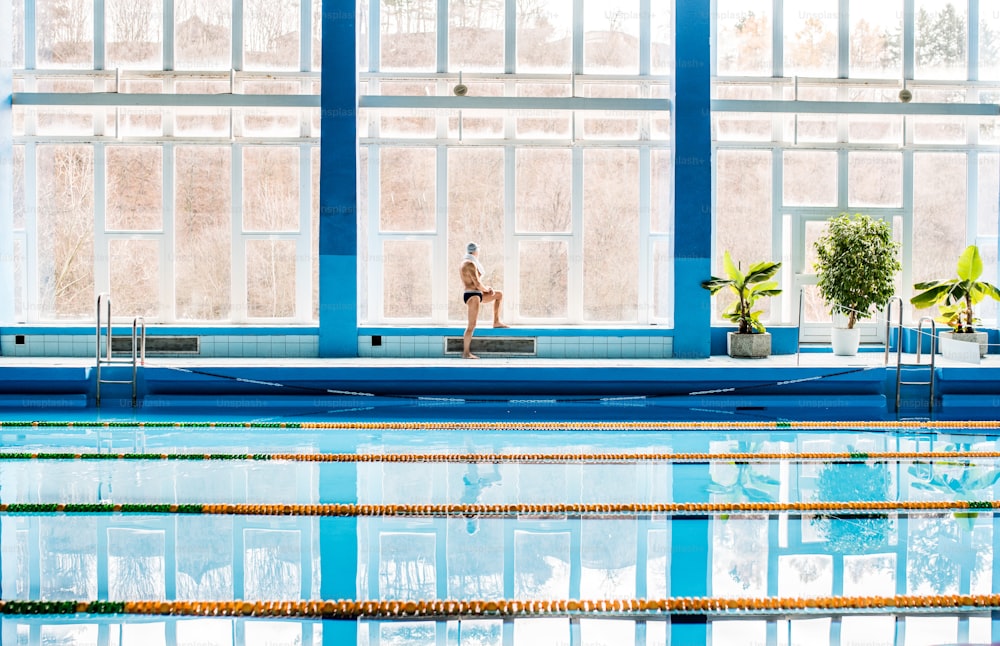 Homme âgé debout au bord de la piscine intérieure. Retraité actif qui fait du sport.