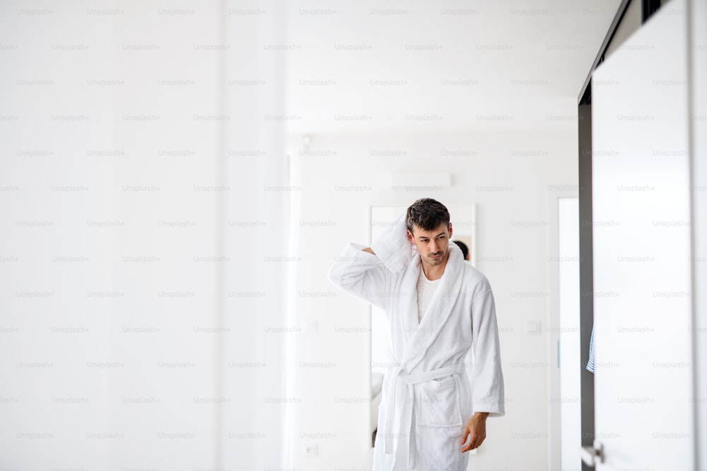 Young man with bathrobe drying hair in the bedroom, a morning routine.