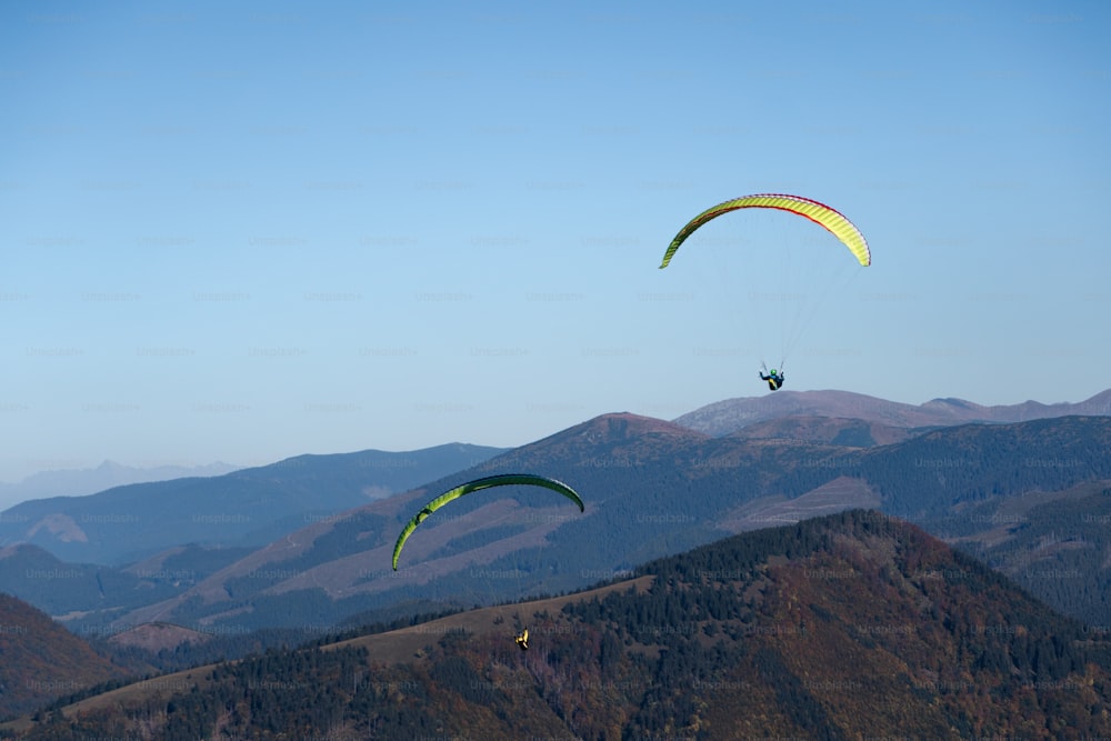 Paragliders flying in a blue sky with mountain in background.