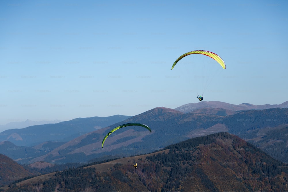 Parapentes volant dans un ciel bleu avec la montagne en arrière-plan.