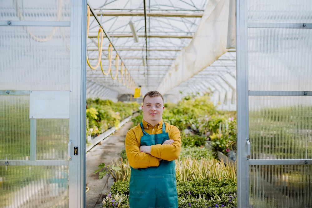Un jeune employé trisomique travaillant dans une jardinerie, regardant la caméra.