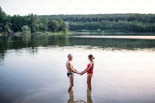 Side view of senior couple in swimsuit standing in lake outdoors before swimming.