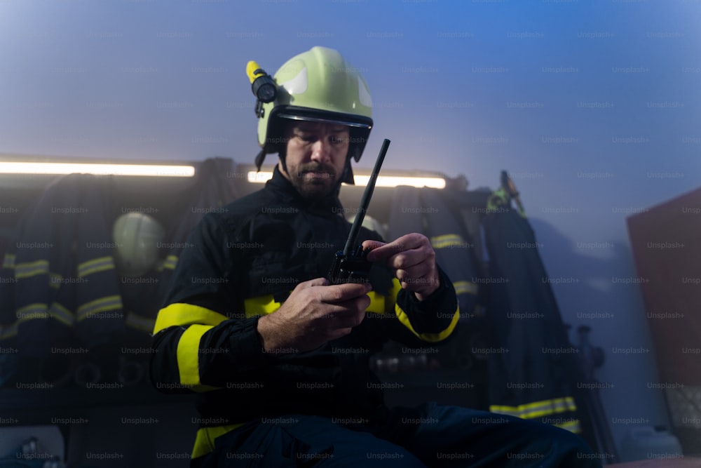 A mature firefighter preparing for action in fire station at night.