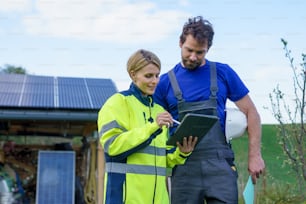 Un uomo e una donna installatori solari ingegneri con tablet durante l'installazione di un sistema di pannelli solari in casa.