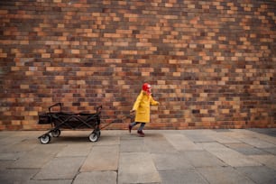 Al ittle Mädchen mit Down-Syndrom zieht den Trolley gegen Ziegelmauer auf der Straße.