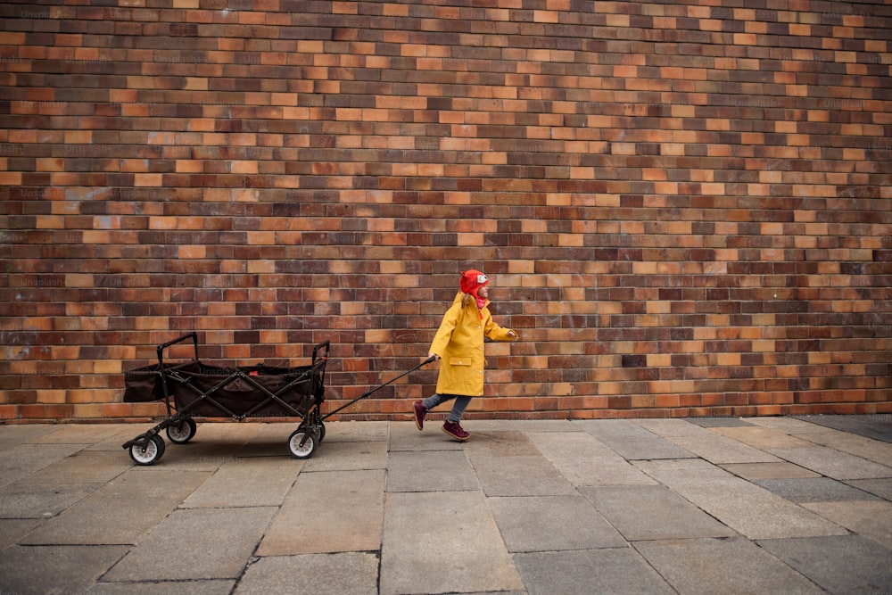 Une petite fille atteinte du syndrome de Down tire le chariot contre un mur de briques dans la rue.
