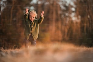 A happy little boy in knitted hoodie having fun on walk in autumn nature.