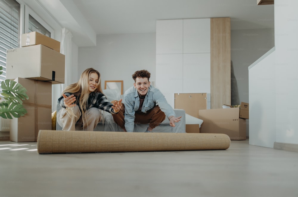 Ein fröhliches junges Paar in ihrer neuen Wohnung rollt Teppich aus. Konzeption des Umzugs.