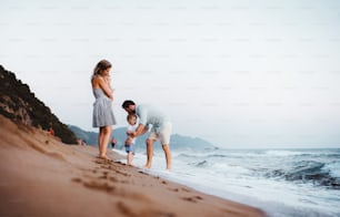 Una familia joven con dos niños pequeños de pie en la playa en vacaciones de verano, divirtiéndose.