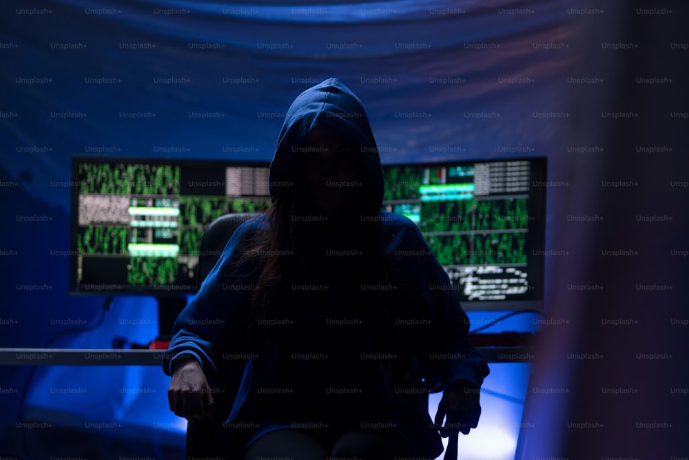 Un hacker anónimo encapuchado por computadora en la habitación oscura por la noche, concepto de guerra cibernética.