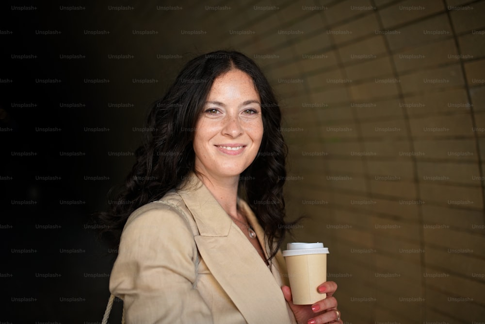 Uma empresária feliz e bem-sucedida que viaja de manhã na rua da cidade, segurando copo de cofee.