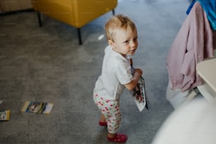 A cute little girl holding book in living room at home.