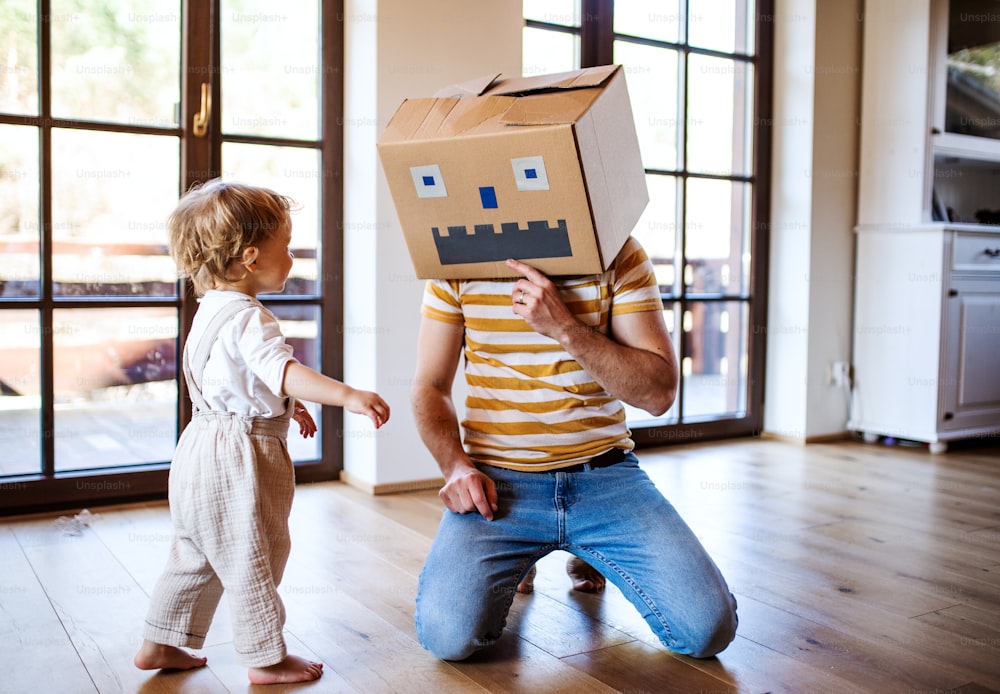 Uma criança feliz com um pai e um monstro de papelão brincando dentro de casa em casa.