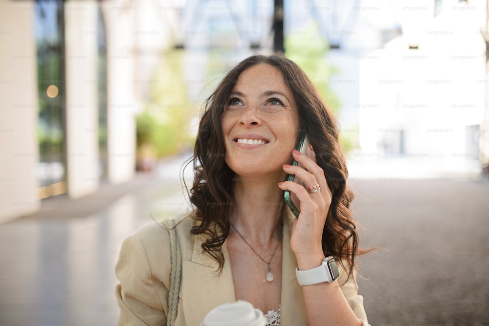 Uma empresária feliz e bem-sucedida que viaja de manhã na rua da cidade, ligando para o celular e segurando o copo de cofee.
