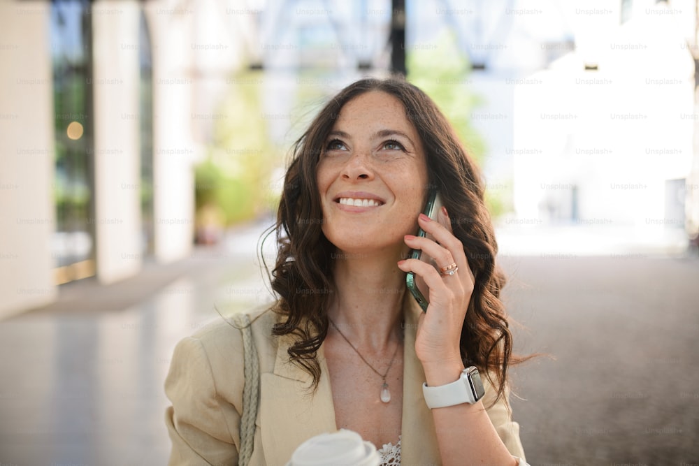 A successful happy businesswoman commuting in the morning in city street, calling on mobile phone and holding cofee cup.