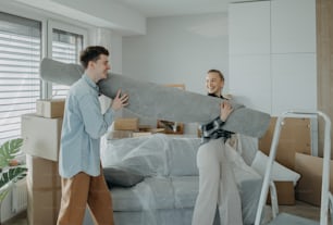 Una alegre pareja joven en su nuevo apartamento, cargando alfombra. Concepción de la mudanza.