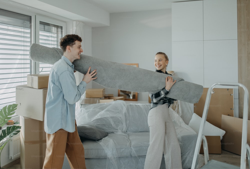 Una alegre pareja joven en su nuevo apartamento, cargando alfombras. Concepción de la mudanza.